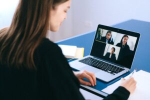 Seorang wanita muda berpakaian profesional sedang menghadiri temuduga online melalui laptop di meja kerja yang kemas.