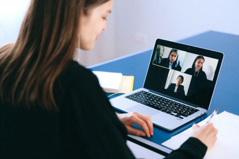 Seorang wanita muda berpakaian profesional sedang menghadiri temuduga online melalui laptop di meja kerja yang kemas.